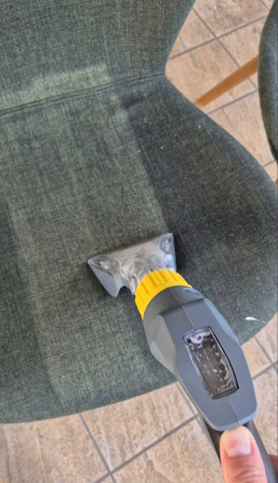 Czyszczenie tapicerki krzesła tekstylnego przy użyciu odkurzacza piorącego. Widoczna różnica w kolorze po praniu. Płytki podłogowe w tle. Ujęcie z góry.