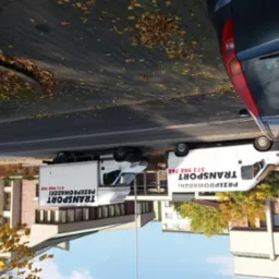 Dwa białe busy z napisem 'Transport Przeprowadzki' zaparkowane obok siebie na ulicy w jesiennej scenerii, z opadłymi liśćmi na chodniku.