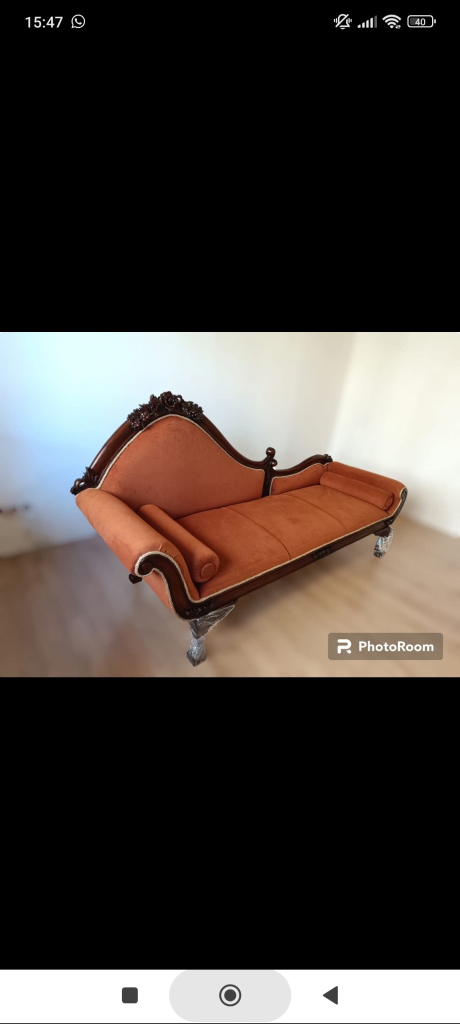 Stylowa leżanka tapicerowana pomarańczową tkaniną, z ciemnego drewna zdobieniami i eleganckimi nóżkami na tle jasnej ściany. Widoczny znak wodny PhotoRoom.