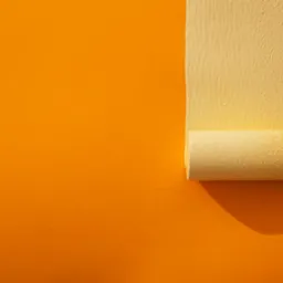 Żółty wałek malarski nanosi farbę na pomarańczową ścianę, tworząc pionowy pas świeżego koloru. Widoczna faktura wałka i farby.