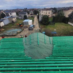 Usb Janek - Montaż łat dachowych i membrany Turbo Premium na nowym dachu, widok z góry na tle zabudowy jednorodzinnej i placu budowy z mini koparką.