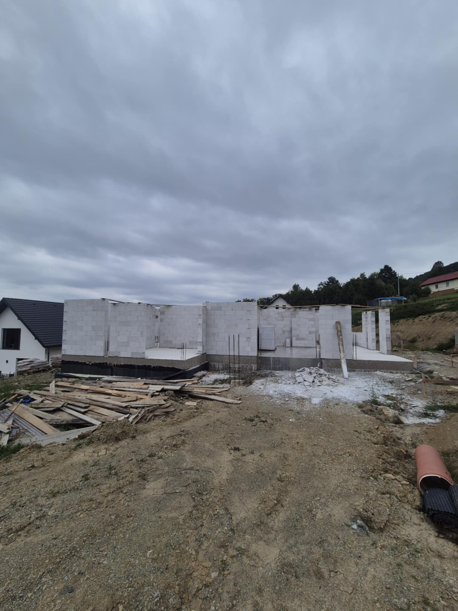 Budowa domu z betonu komórkowego: widok na wzniesione ściany parteru, z widocznym zbrojeniem. Na pierwszym planie składowane deski i gruz.