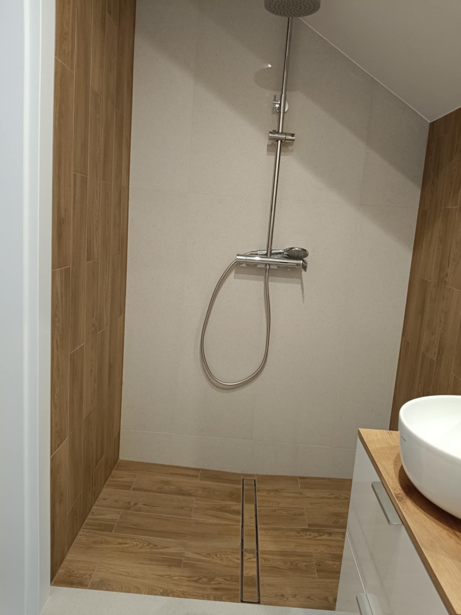 Nowoczesna kabina prysznicowa walk-in z odpływem liniowym i drewnopodobnymi płytkami na ścianach oraz podłodze, z deszczownicą i baterią termostatyczną.