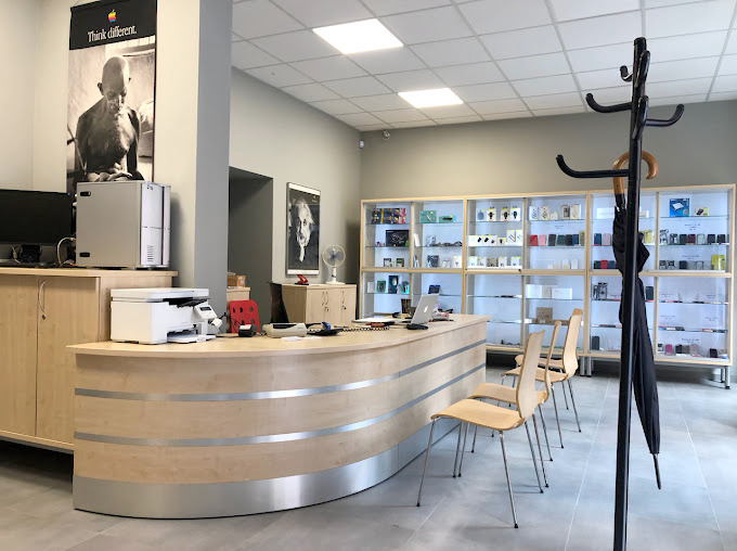 Wnętrze serwisu: lada recepcyjna z komputerem, drukarką i laptopem. W tle gabloty z akcesoriami do telefonów, plakat z Gandhim i portret Einsteina.