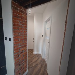 Aproxaa - Wykończenie wnętrza: odnowione przejście z odsłoniętą czerwoną cegłą, kontrastujące z gładkimi, białymi ścianami i nowymi drzwiami z przeszkleniami. Nowoczesne oświetlenie.