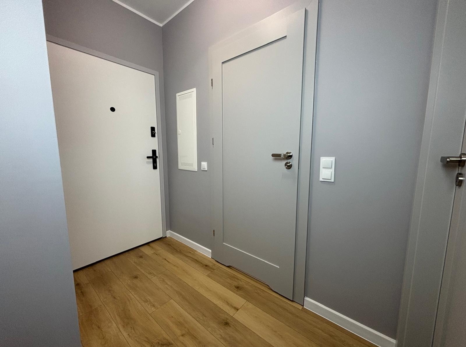 Szare ściany, drewnopodobne panele i dwie białe, nowoczesne drzwi wewnętrzne z srebrnymi klamkami w przedpokoju po remoncie.