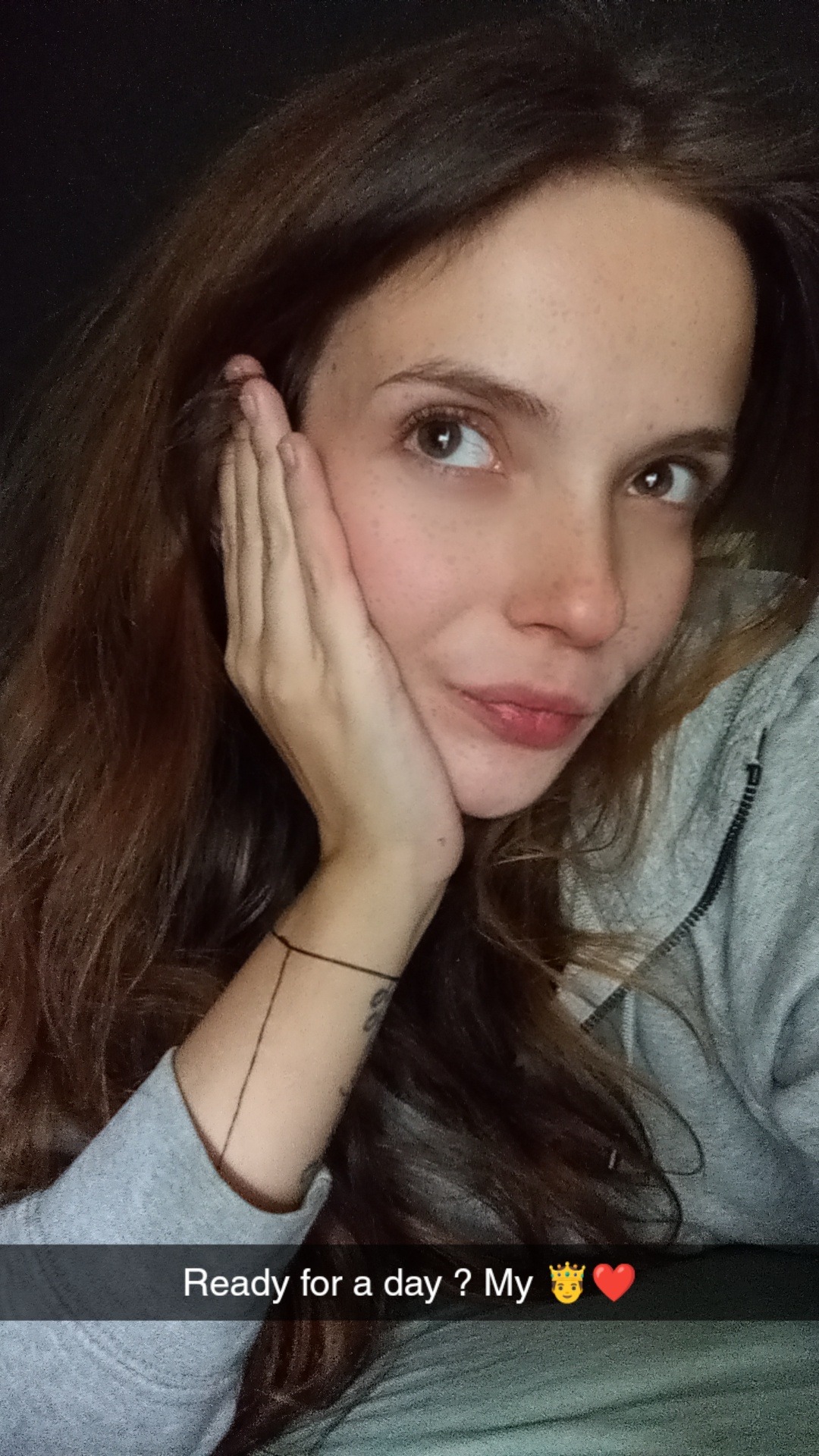 Portret kobiety z brązowymi włosami, opierającej policzek na dłoni, z widocznym tatuażem na przedramieniu. Ujęcie z dołu, skierowane ku górze.