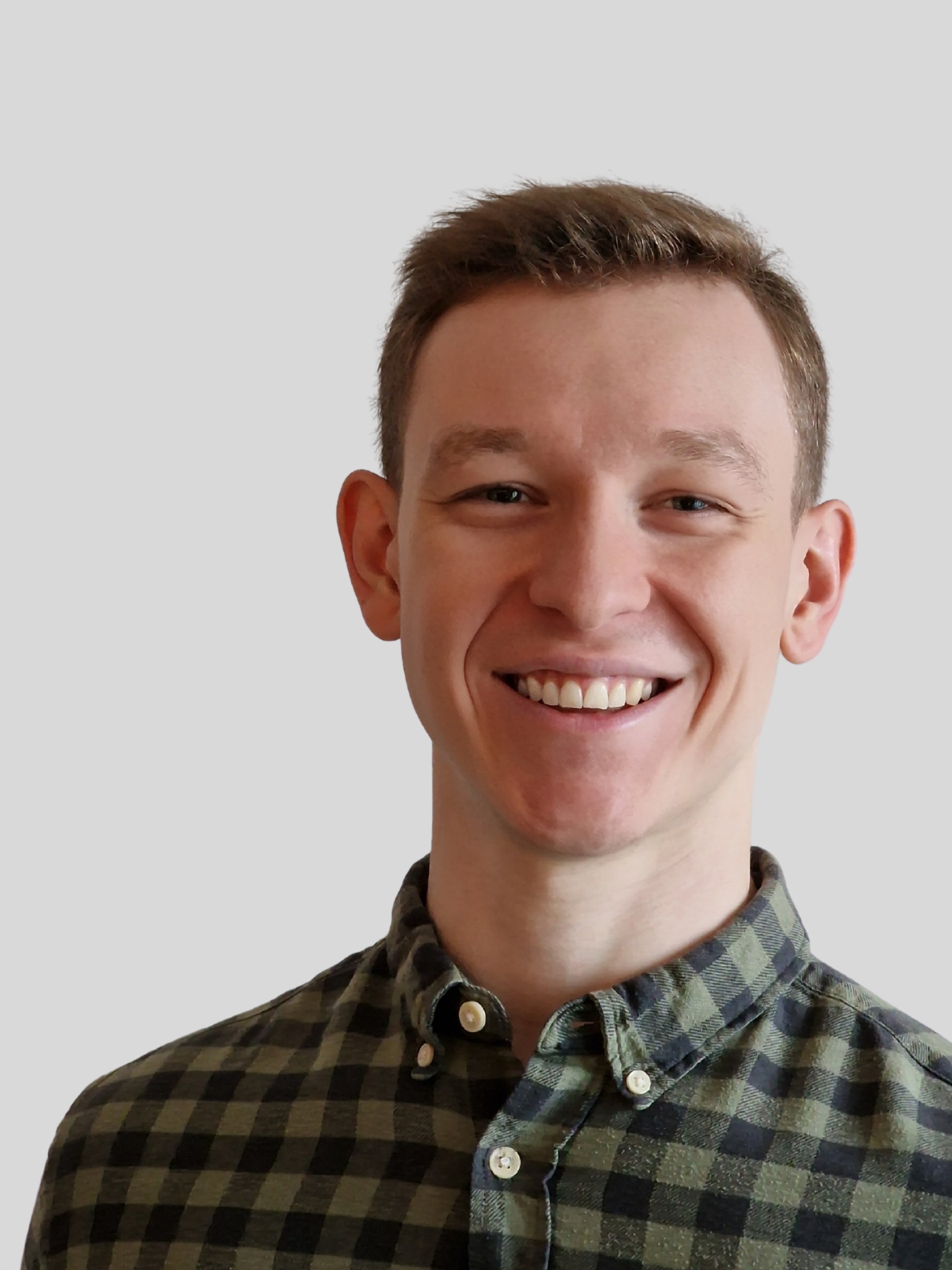 Uśmiechnięty mężczyzna w zielonej koszuli w kratę, portret z bliska na jasnoszarym tle. Widoczne detale twarzy i faktura materiału koszuli.