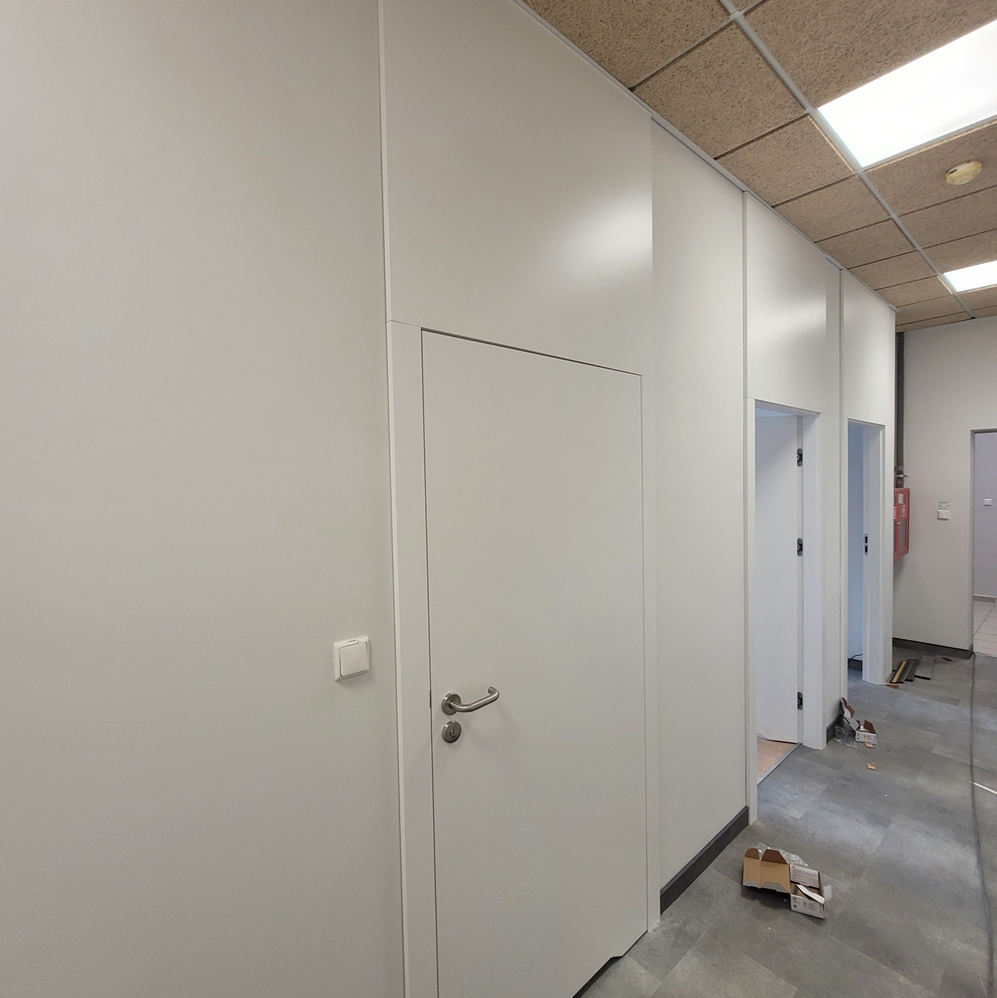 Białe, modułowe ściany biurowe po remoncie z ukrytymi drzwiami i widocznymi elementami wykończeniowymi na podłodze. Widok na korytarz.