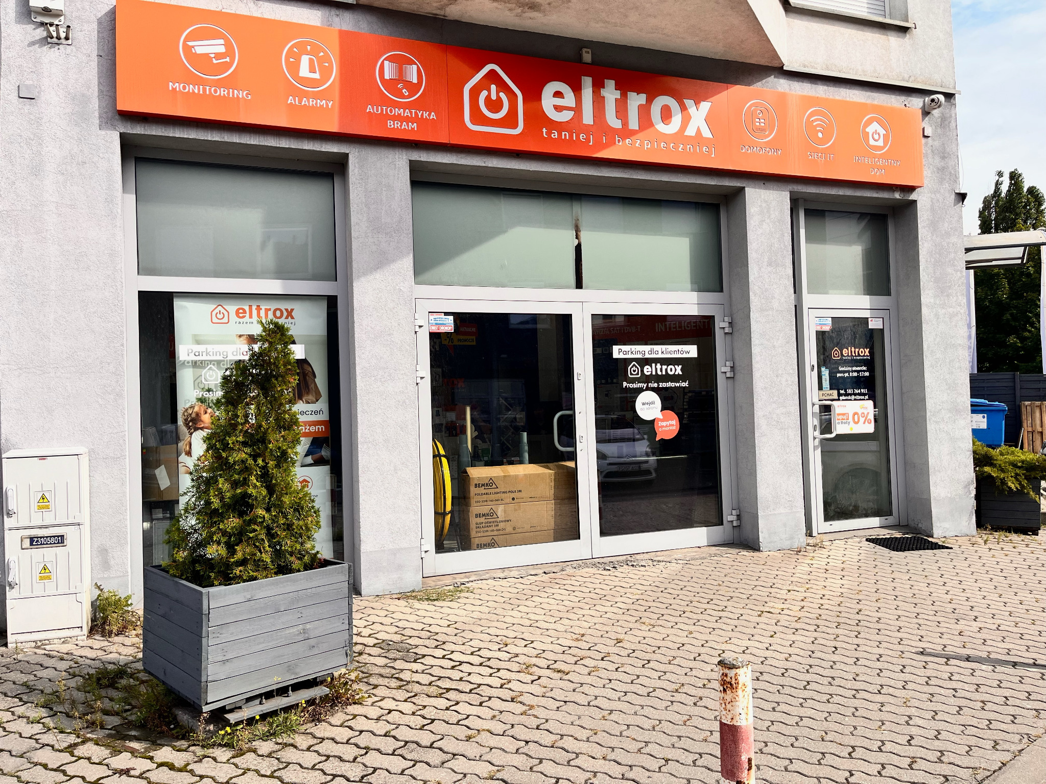 Fasada sklepu Eltrox z monitoringiem, alarmami, automatyką bram i inteligentnym domem. Pomarańczowy szyld z logo nad wejściem.