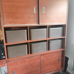 ULMAN - Regał z przesuwnymi drzwiami i półkami z koszami w Koszalinie. Mebel z drewna w odcieniach brązu, widoczne detale wykończenia i metalowe uchwyty.