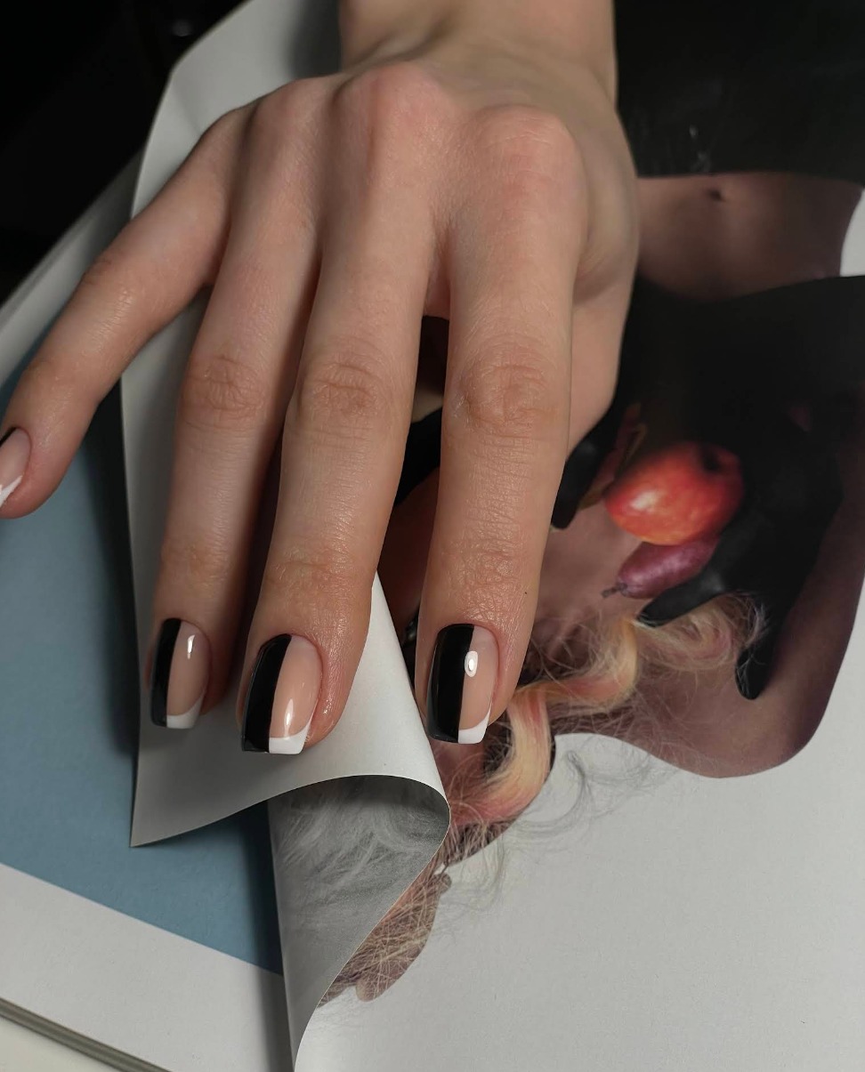 Dłoń z manicure: czarne pionowe pasy i białe końcówki na krótkich paznokciach. Dłoń trzyma otwartą stronę magazynu.