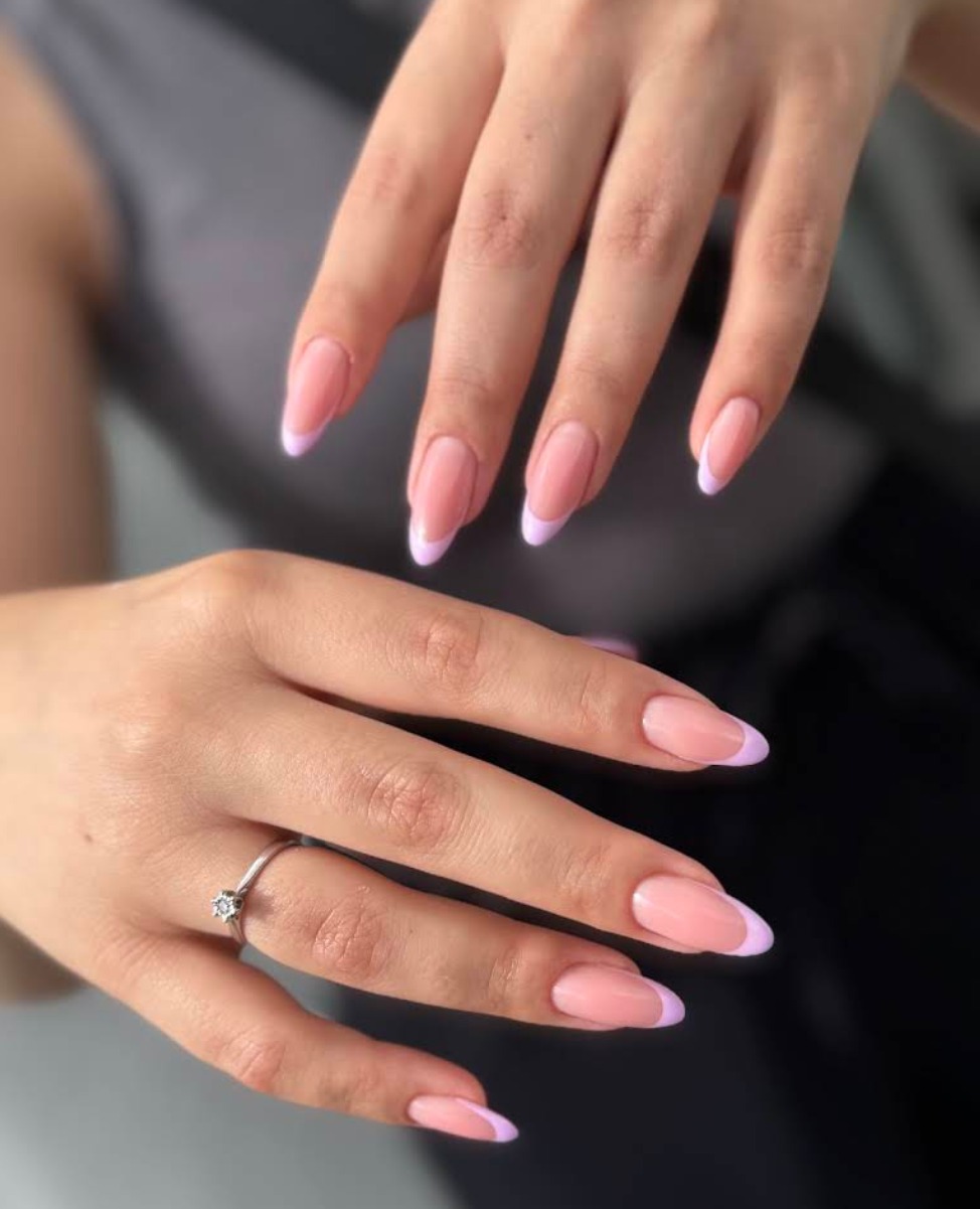 Delikatny french manicure z fioletowymi końcówkami na dłoni z pierścionkiem. Subtelny, elegancki wygląd paznokci.