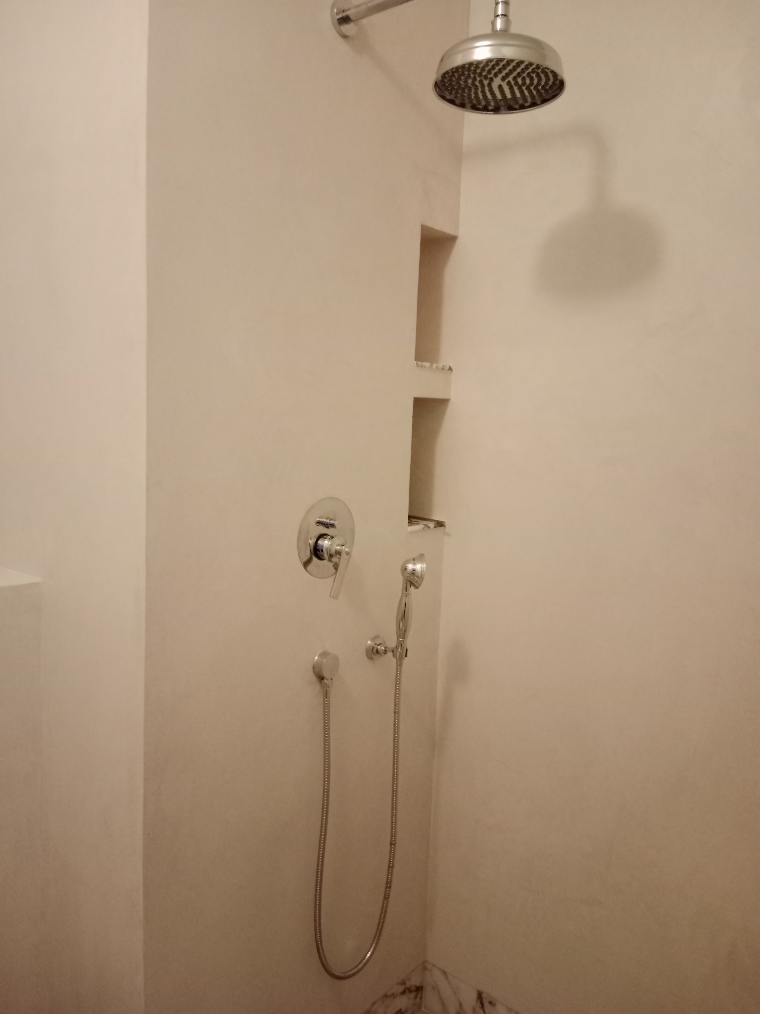 Nowoczesna kabina prysznicowa z deszczownicą i wnęką w ścianie, wykończona w jasnych, stonowanych barwach. Minimalistyczny design, chromowana armatura.