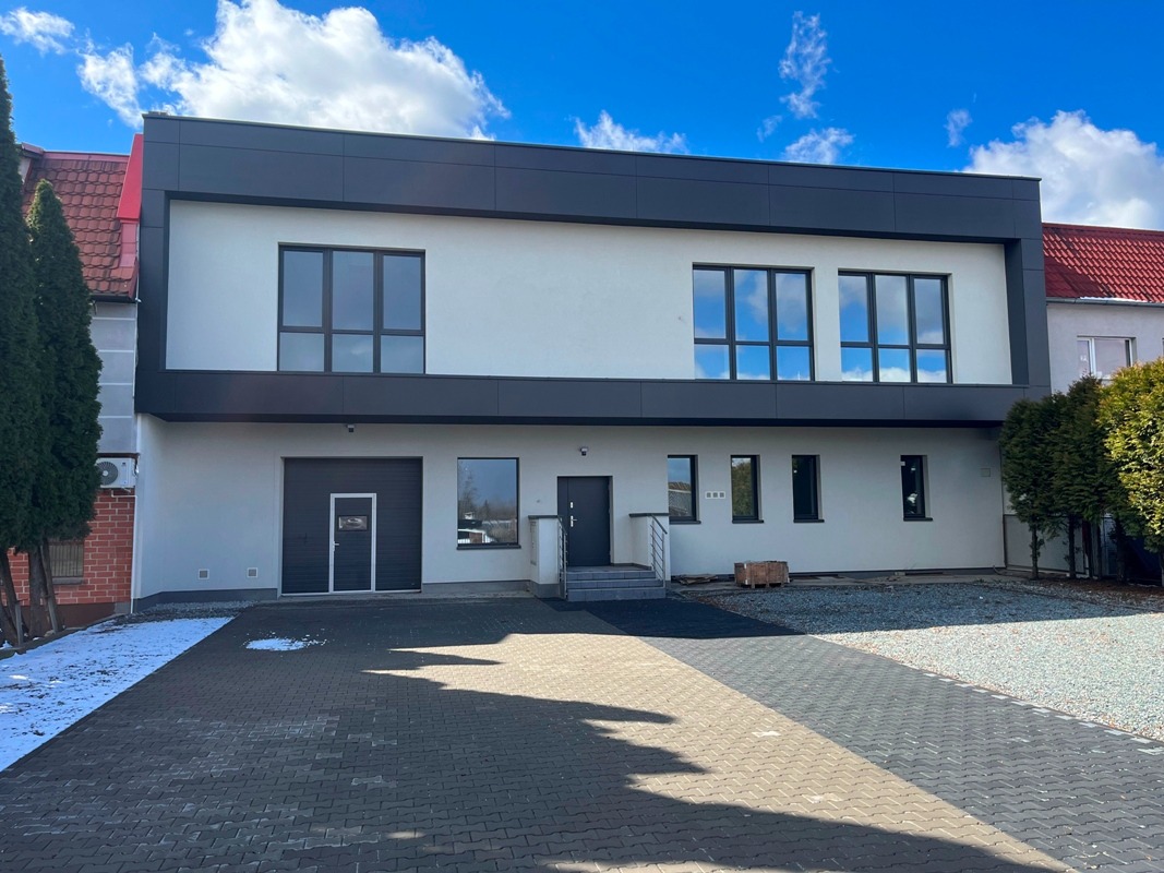 Nowoczesny budynek biurowy z czarno-białą elewacją i dużymi oknami, widok z zewnątrz, kostka brukowa przed budynkiem, błękitne niebo.