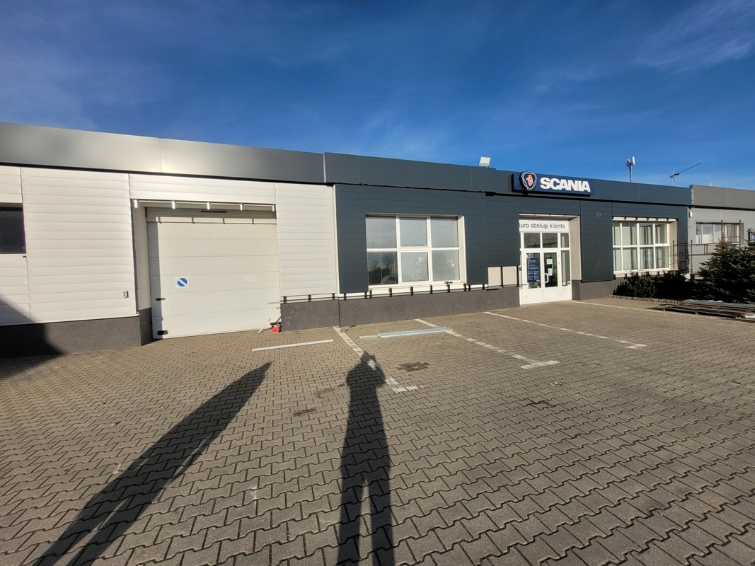 Nowoczesna hala w stonowanej kolorystyce we Wrocławiu. Widoczna brama garażowa i wejście do biura obsługi klienta. Na dachu logo Scania.