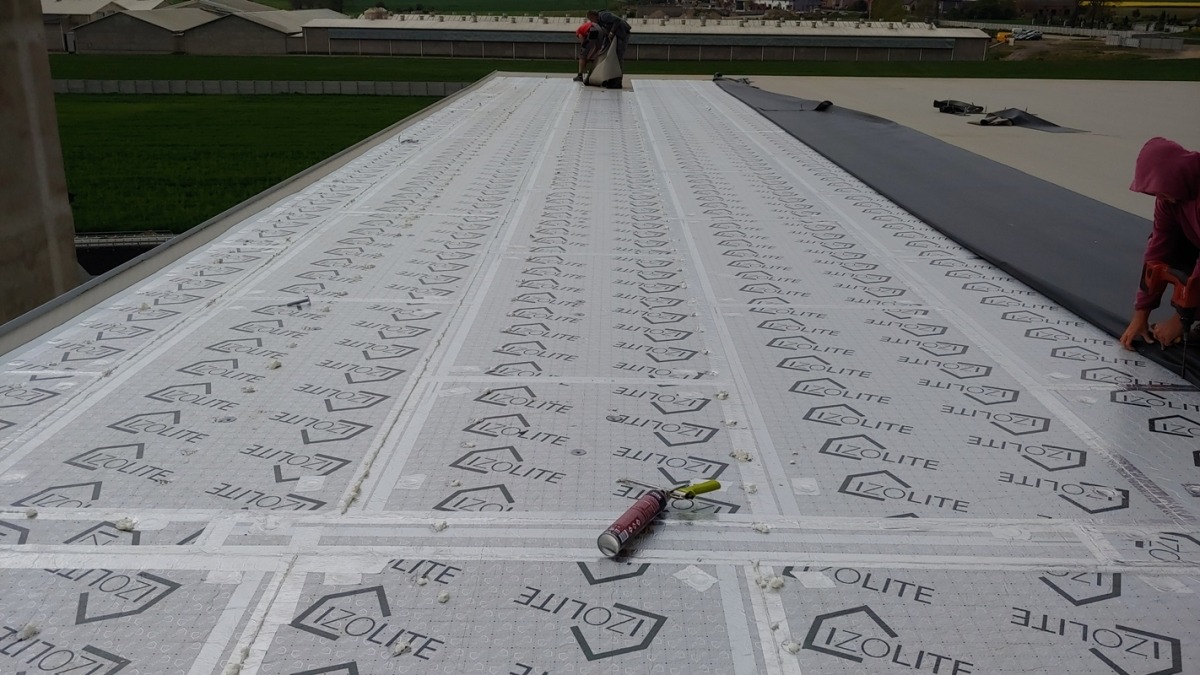 Montaż izolacji termicznej IZOLITE na dachu hali przemysłowej, widoczni pracownicy i narzędzia. Etap prac przed położeniem finalnego pokrycia dachowego.