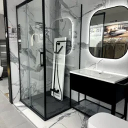 Nowoczesna łazienka: kabina prysznicowa z czarną ramą, umywalka z podświetlanym lustrem i toaleta na tle marmurowych płytek podłogowych i ściennych.