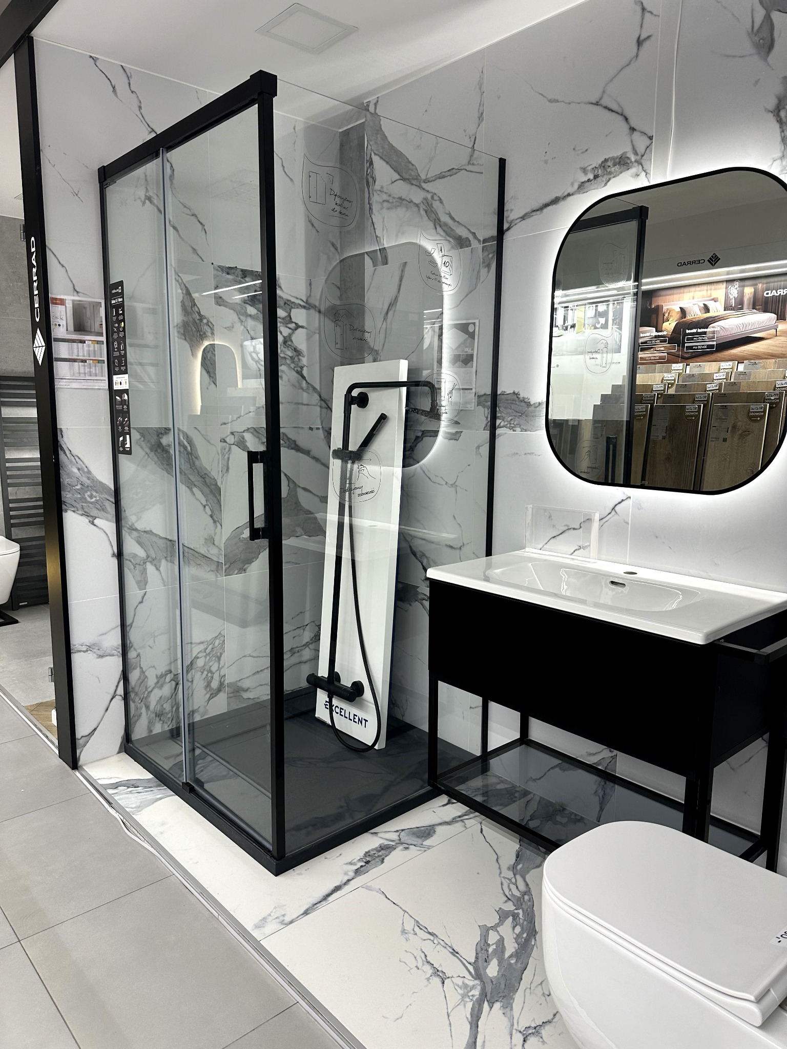 Nowoczesna łazienka: kabina prysznicowa z czarną ramą, umywalka z podświetlanym lustrem i toaleta na tle marmurowych płytek podłogowych i ściennych.