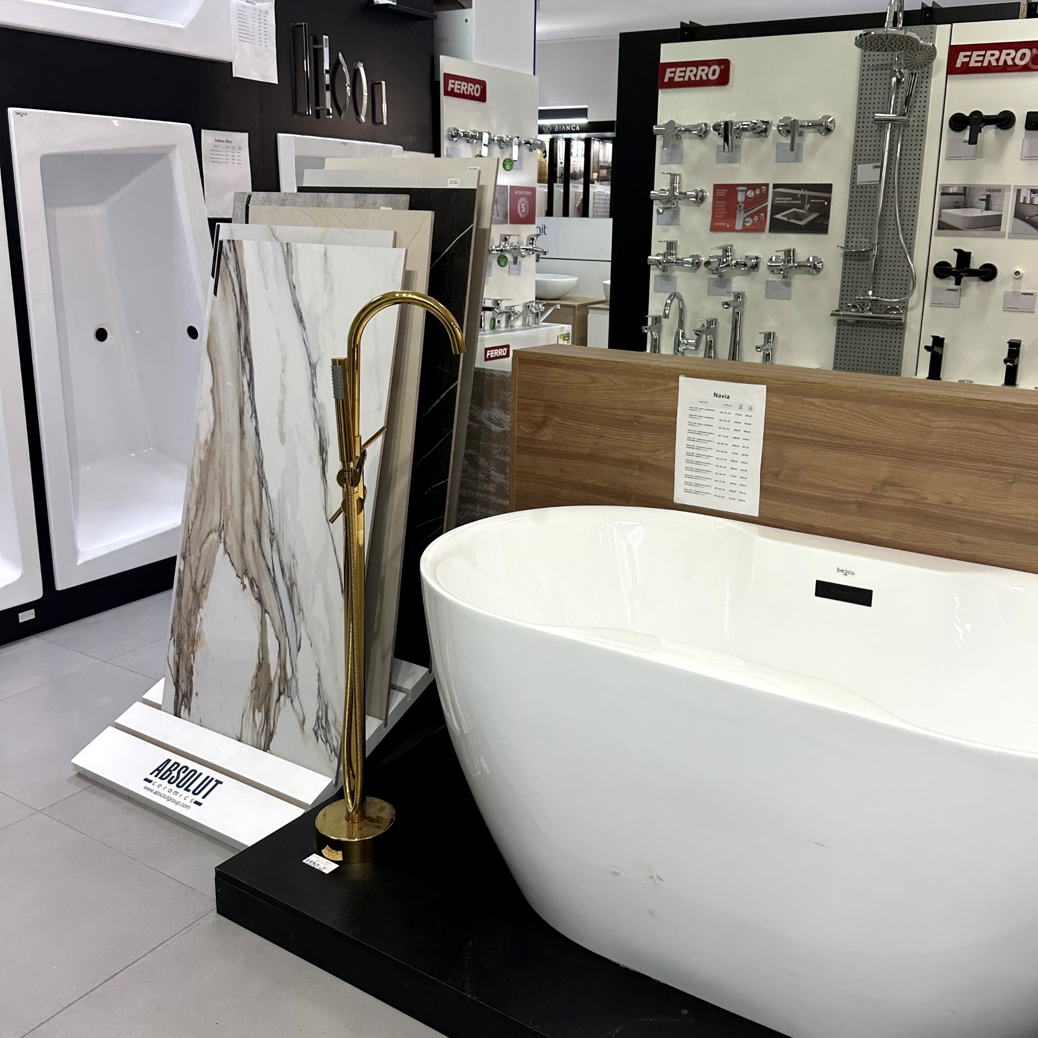 Ekspozycja łazienki: owalna wanna wolnostojąca, złota bateria podłogowa, płytki imitujące marmur. Armatura Ferro w tle. Aranżacja sklepu z wyposażeniem łazienek.