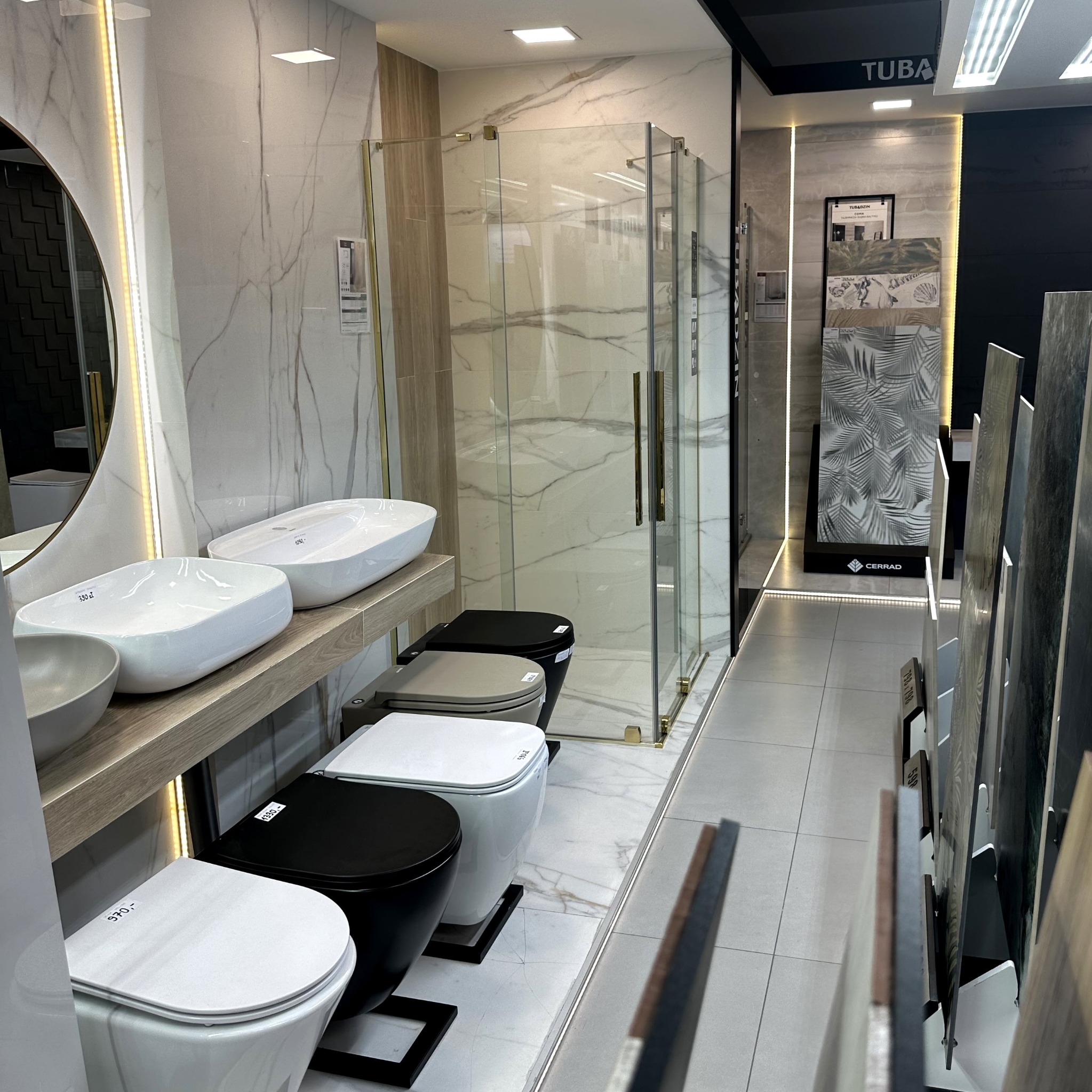 Salon łazienek: ekspozycja z umywalkami na blacie, kabiną prysznicową i panelami ściennymi. Widoczne ceny na armaturze.