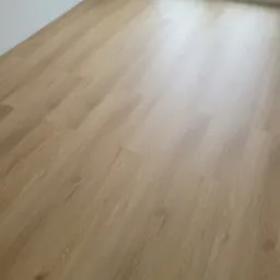 Jasne panele podłogowe ułożone w nowym pomieszczeniu z białymi ścianami i oknem, przez które widać zieleń. Widok z góry, bliski kadr.