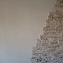 Ściana z dekoracyjną okładziną kamienną w odcieniach bieli i beżu, kontrastująca z gładką, pomalowaną powierzchnią. Widoczny fragment podłogi.