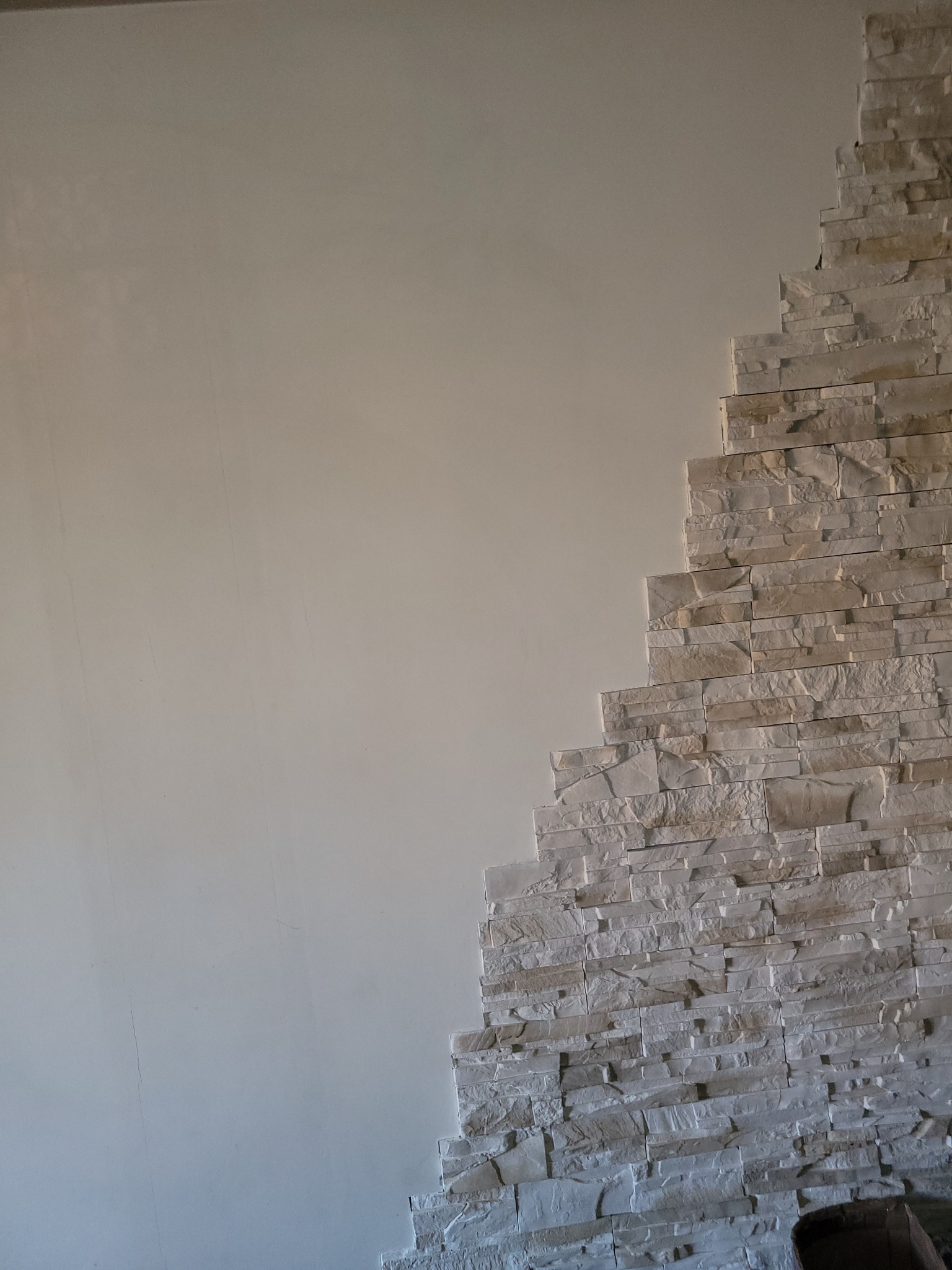 Ściana z dekoracyjną okładziną kamienną w odcieniach bieli i beżu, kontrastująca z gładką, pomalowaną powierzchnią. Widoczny fragment podłogi.