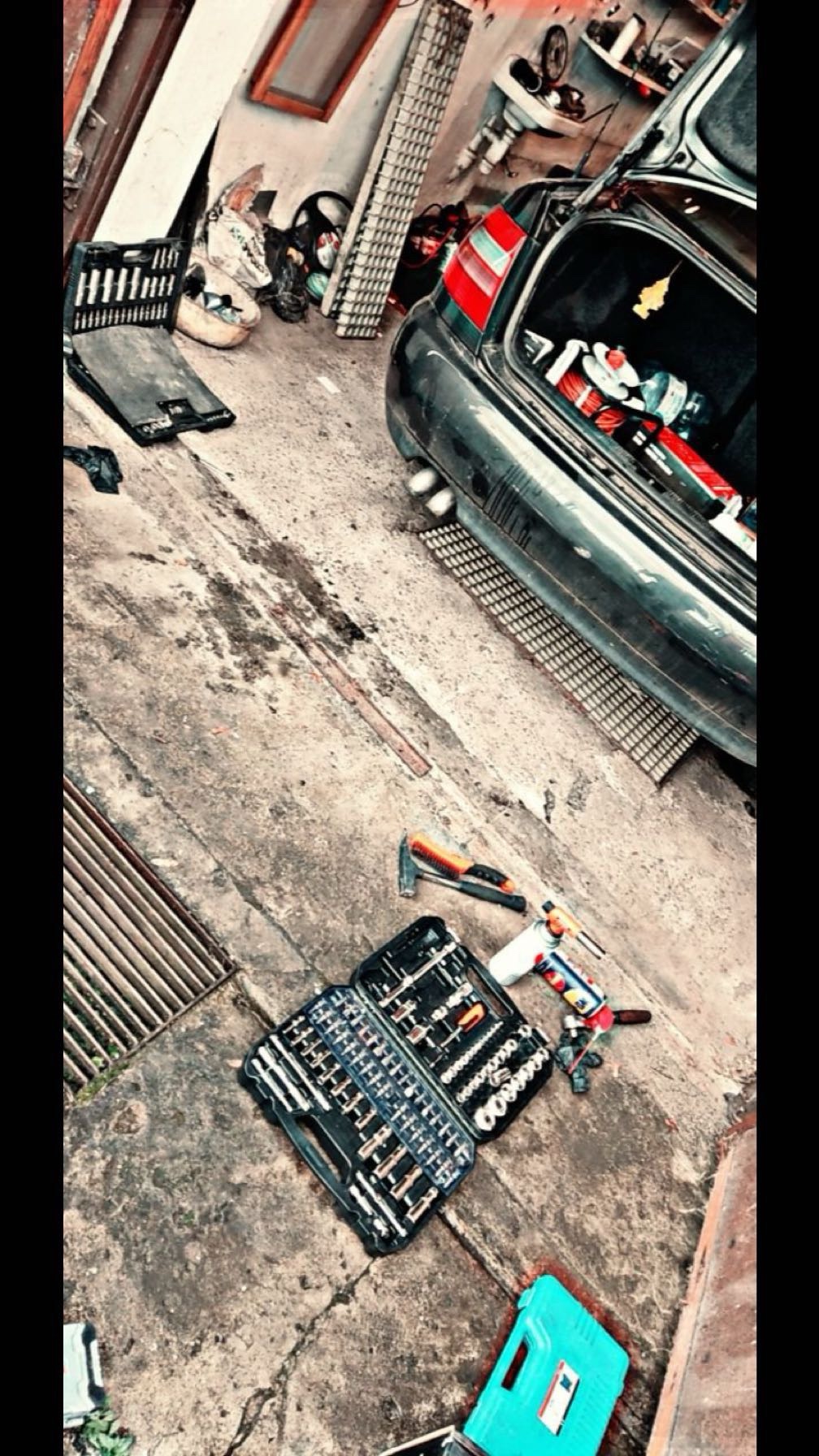 Otwarty bagażnik auta, skrzynka z narzędziami, młotek i butla gazowa na betonowej posadzce w warsztacie. Sprzęt i akcesoria samochodowe.