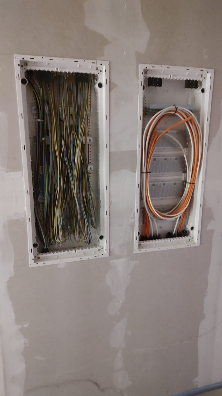 Dwie podtynkowe skrzynki elektryczne z przewodami w ścianie przed wykończeniem, widoczne różnokolorowe kable i przewody pomarańczowo-białe.