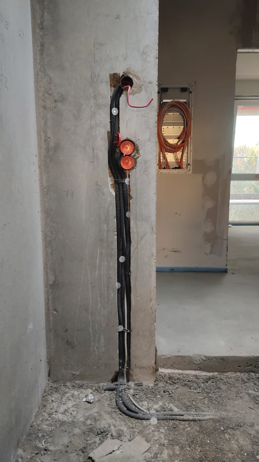 Ściana w trakcie prac instalacyjnych: peszle z przewodami elektrycznymi prowadzone wzdłuż ściany, widoczna puszka instalacyjna w głębi pomieszczenia.