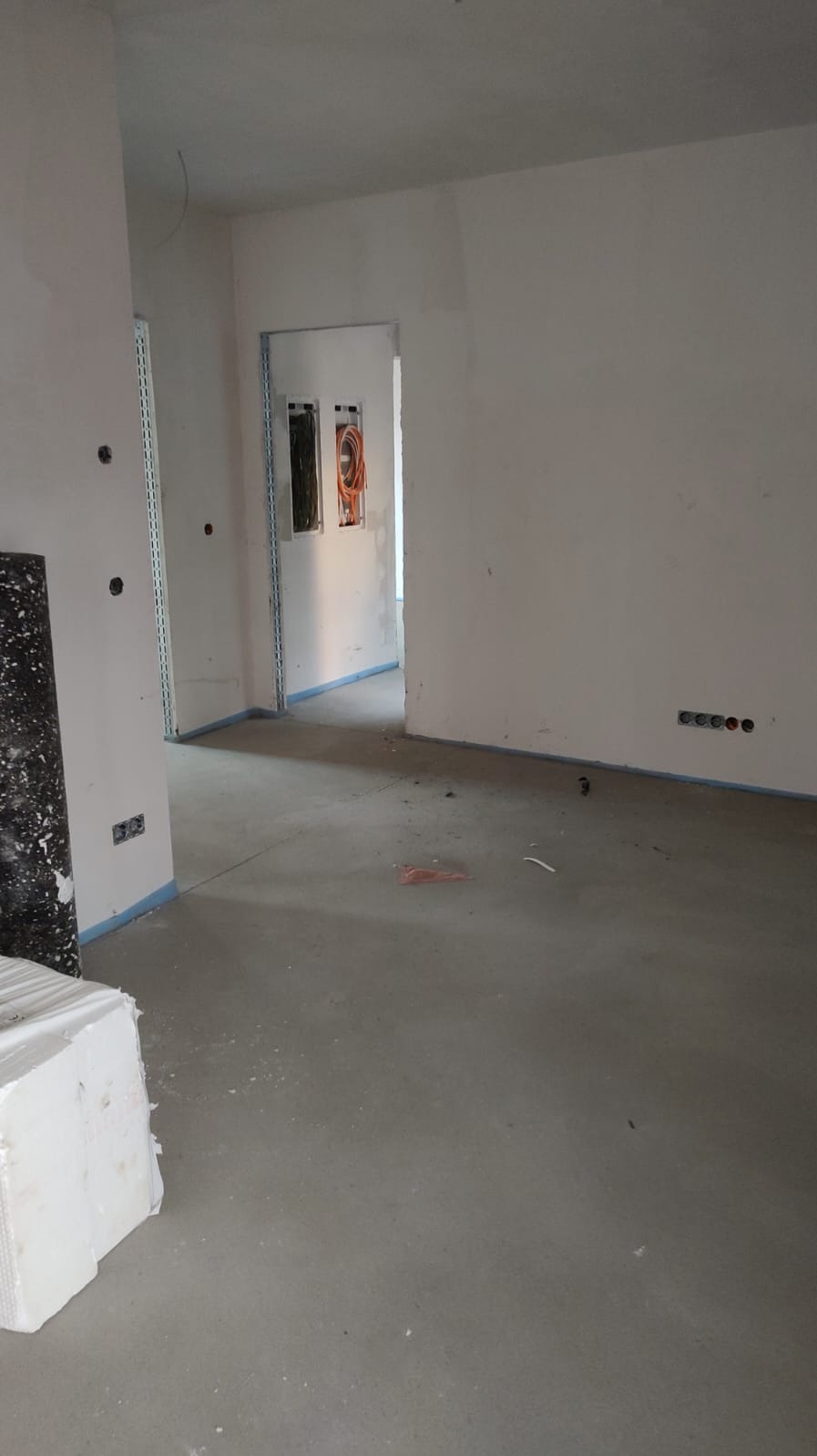 Wnętrze w stanie surowym: ściany z instalacją elektryczną w peszlach, gniazdka, wylewka betonowa. Widoczne przygotowania do dalszych prac wykończeniowych.