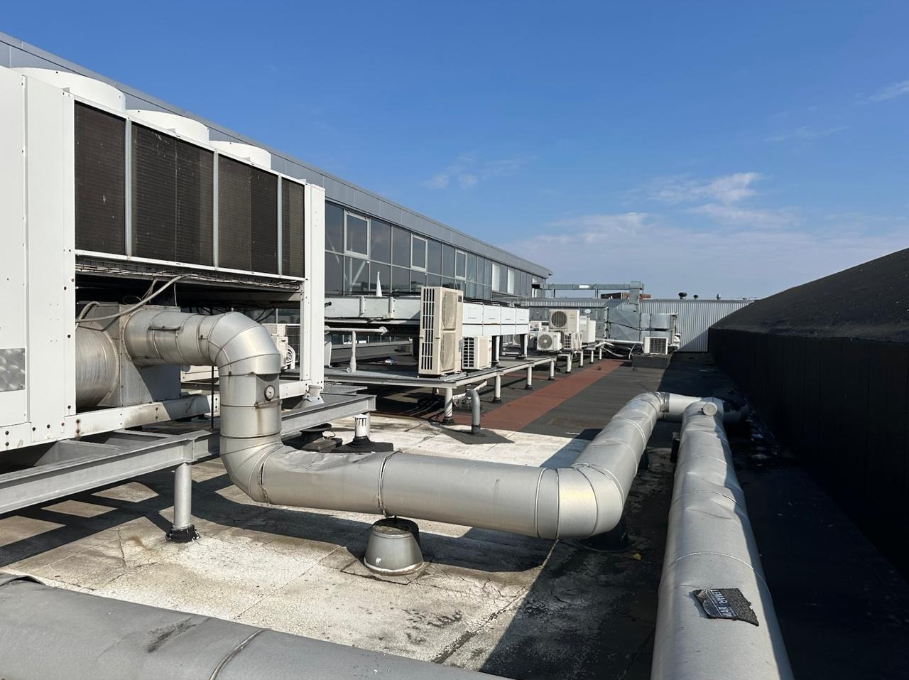 Instalacja klimatyzacji przemysłowej na dachu budynku z widocznymi rurami i jednostkami zewnętrznymi pod błękitnym niebem. Widok z perspektywy.