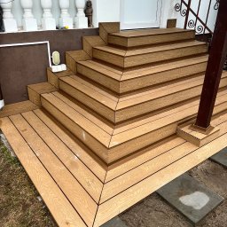 Dach i Dech Zapiera Norbert Staszewski - Schody wejściowe wyłożone deską kompozytową w odcieniach brązu, prowadzące do drzwi. Widoczne balustrady i elementy dekoracyjne budynku. Estetyczne wykończenie.