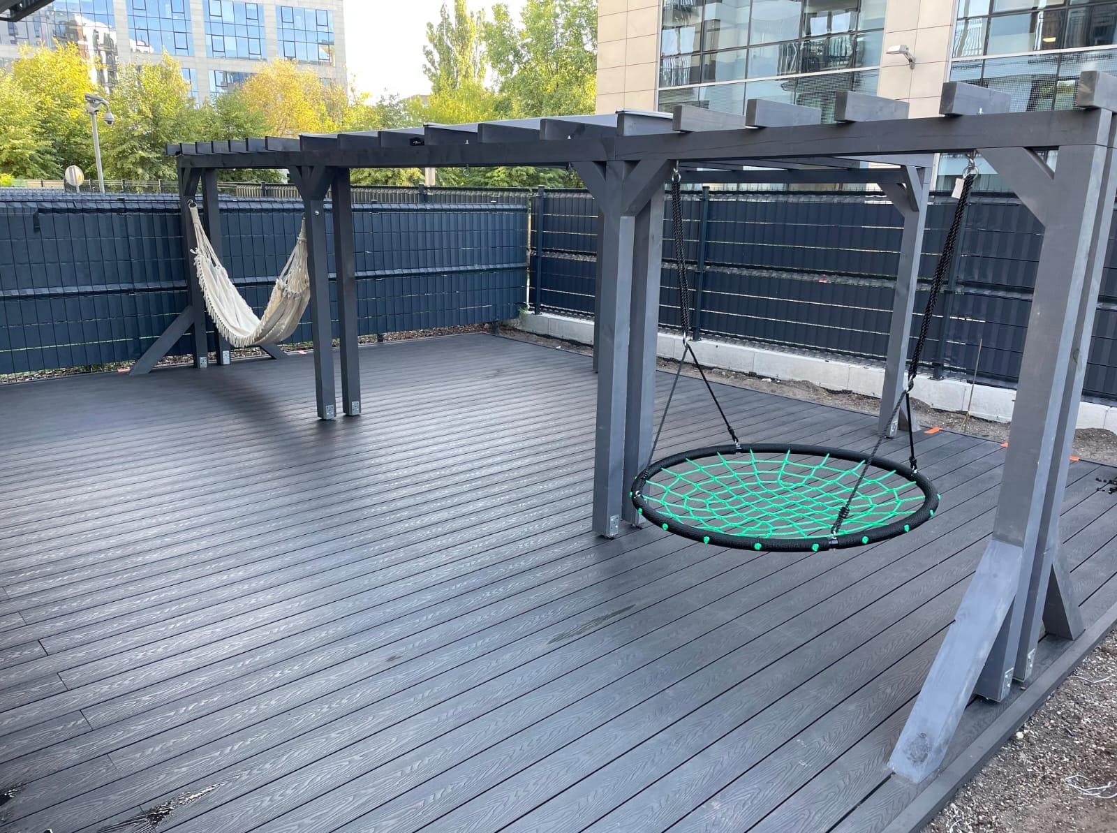 Nowoczesny taras kompozytowy z pergolą i huśtawką w Warszawie. Deska w odcieniach szarości, minimalistyczny design. Hamak dodaje przytulności.