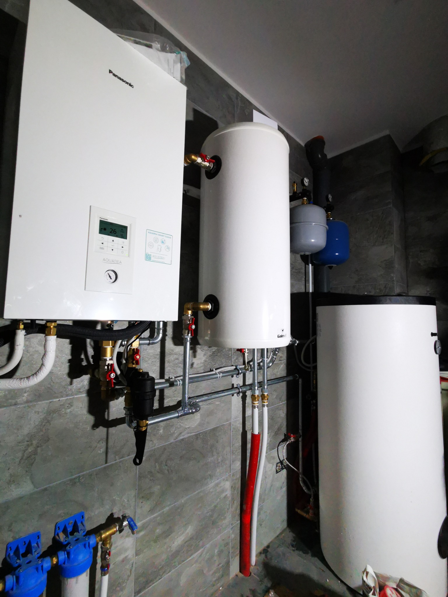 Nowoczesna kotłownia z podgrzewaczem wody i filtrami w Kurzelowie. Białe urządzenia na tle szarej ściany, widoczne rury i zawory.