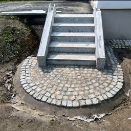 SobBruk Wiesław Sobczyk - Granitowe schody z półokrągłym brukowanym placem. Kostka granitowa ułożona w wachlarzowy wzór. Widoczne ślady zaprawy i prac ziemnych.