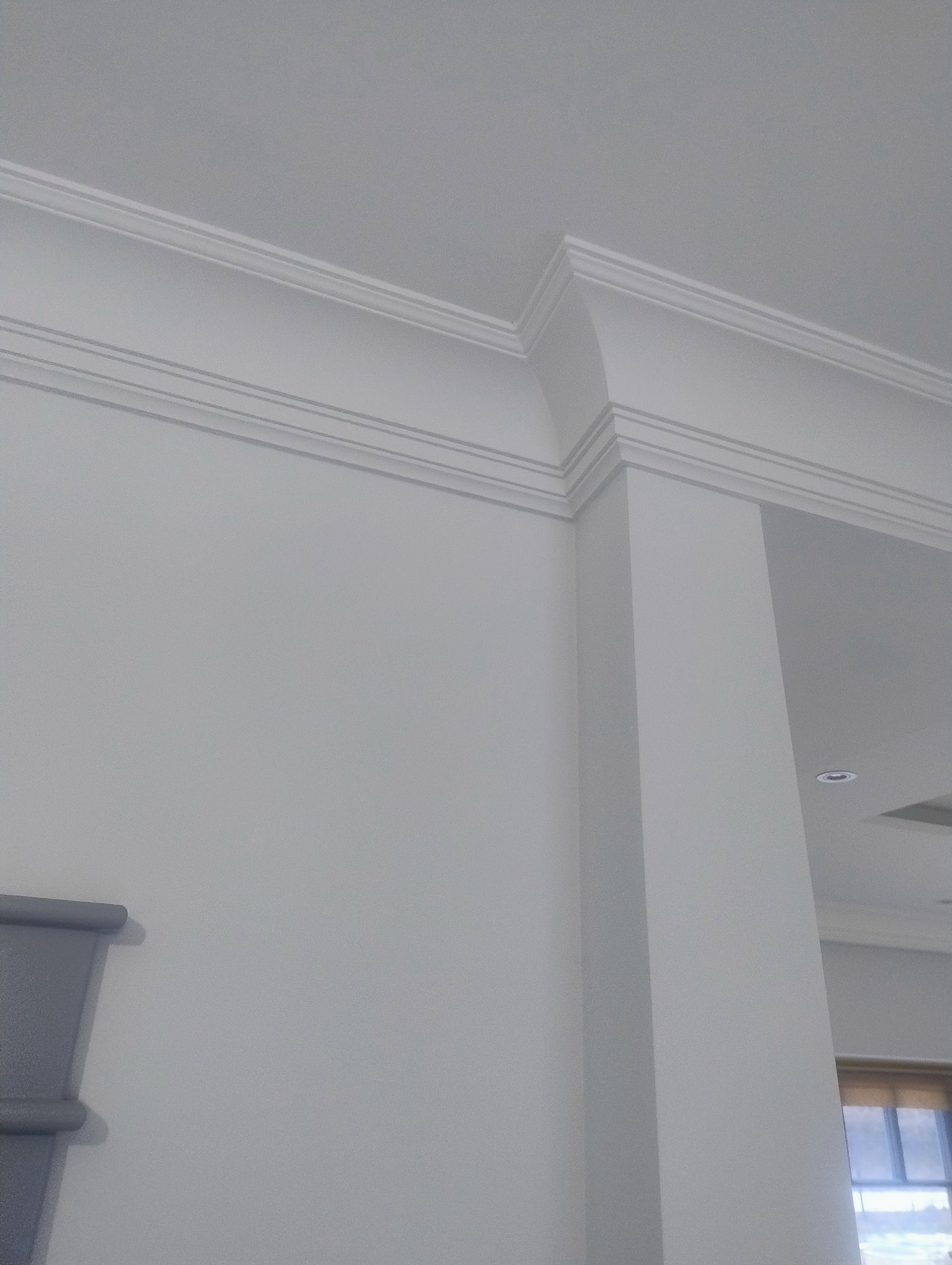 Białe, eleganckie listwy dekoracyjne na styku ściany i sufitu, tworzące estetyczne wykończenie wnętrza. Widoczny fragment ściany i kolumna.