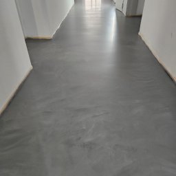 LuxFloors Arkadiusz Tomaszewski - Szara, gładka posadzka w długim korytarzu z białymi ścianami, widok z perspektywy, delikatne refleksy światła na powierzchni podłogi.