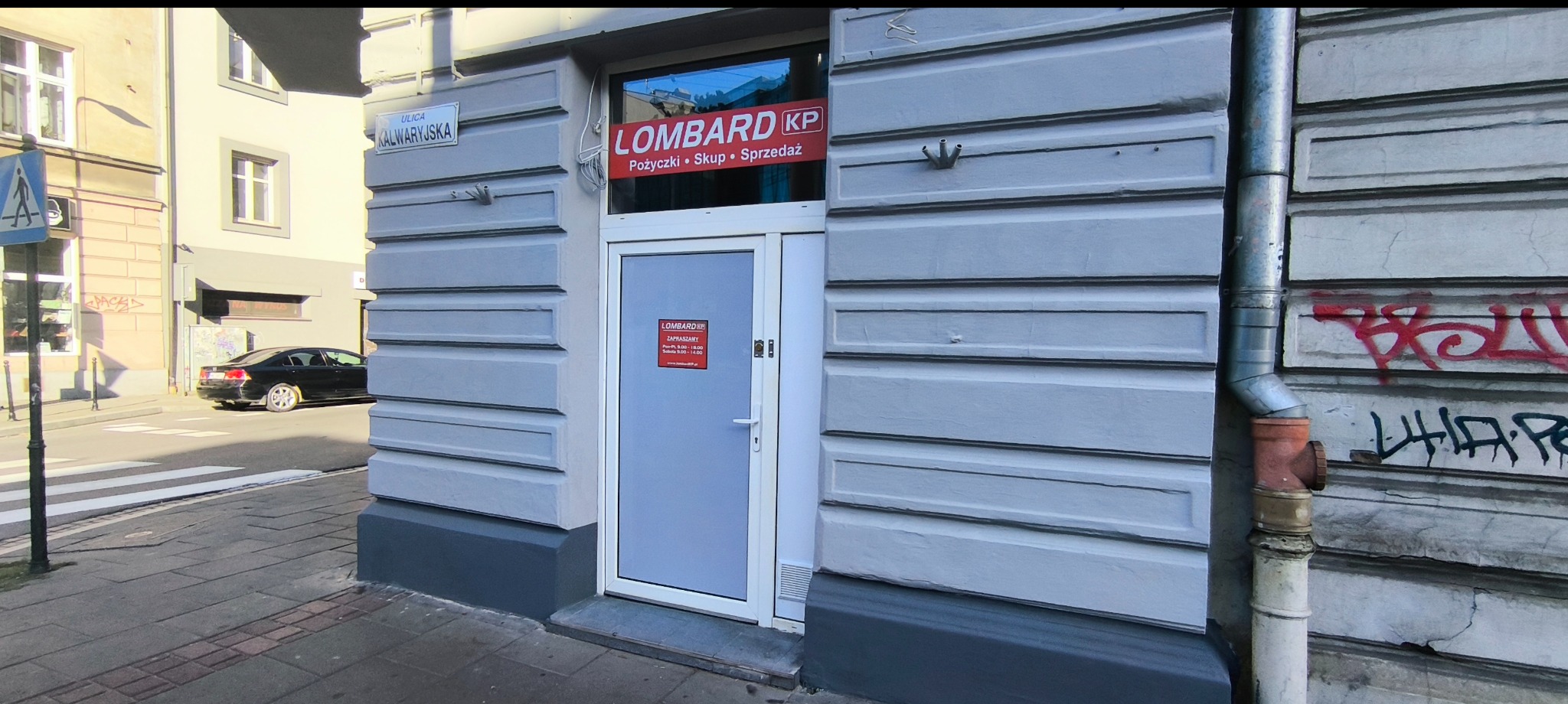 Wejście do lombardu z szyldem LOMBARD KP, oferta: pożyczki, skup, sprzedaż. Na ścianie budynku widoczna nazwa ulicy: Kalwaryjska.