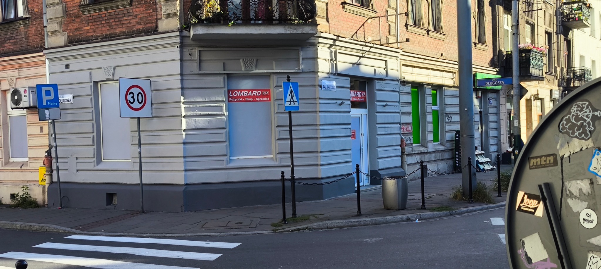 Budynek narożny z szyldem 'Lombard KP'. Widoczne znaki drogowe, ulica Jana Długosza i Kalwaryjska. Pożyczki pod zastaw.
