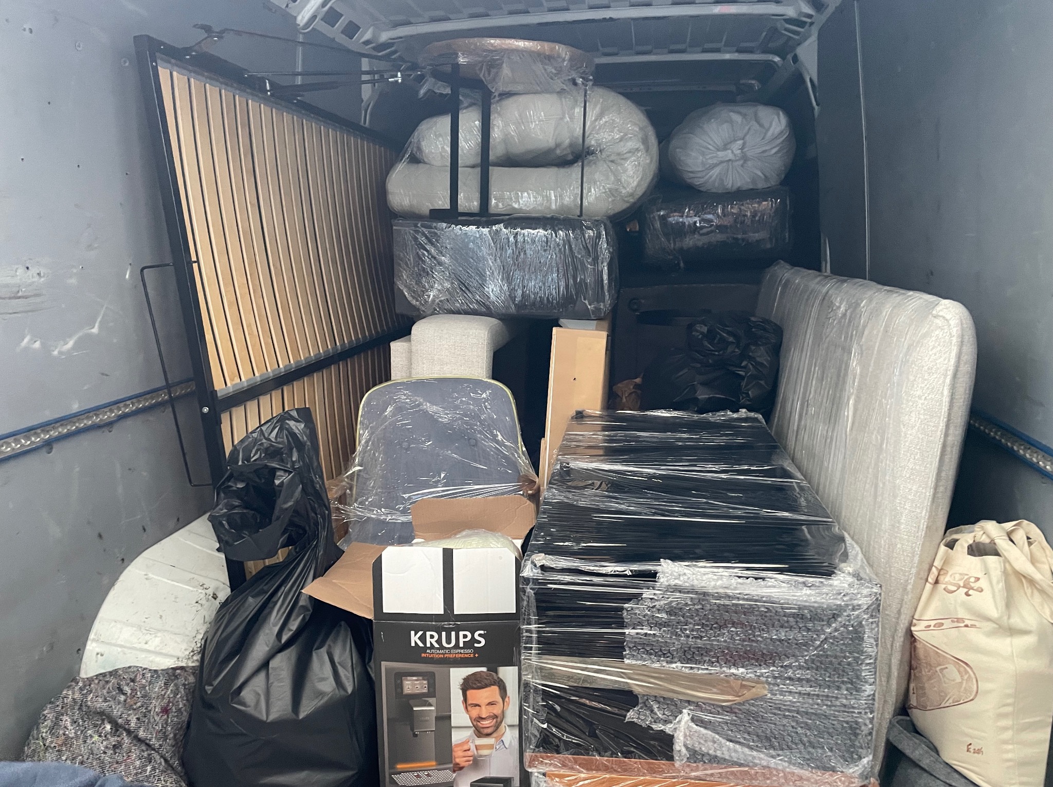 Wnętrze busa wypełnione po brzegi meblami i sprzętami, zabezpieczonymi folią stretch, gotowymi do transportu. Widoczny stelaż łóżka, krzesła, pudła i pakunki.