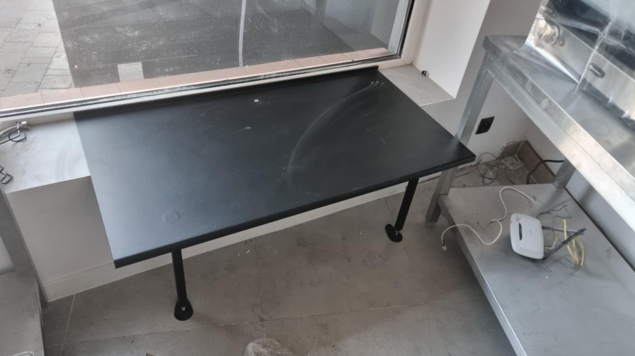 Czarny, metalowy blat przymocowany do parapetu, z nogami. Obok widoczny metalowy stół i router. Wykonanie ślusarskie na wymiar, nowoczesny design.