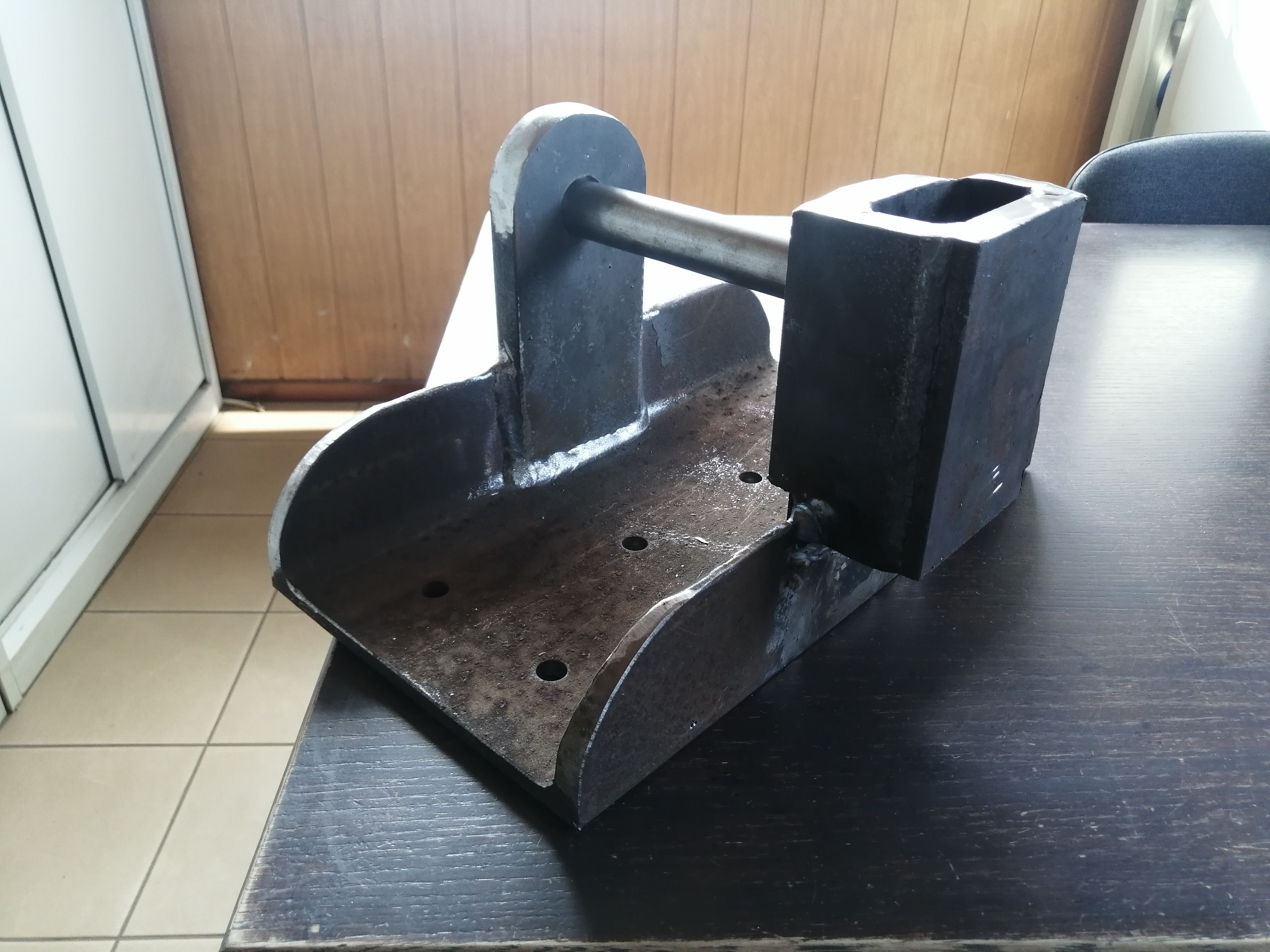 Metalowa konstrukcja spawana, z widocznymi śladami spawania, na ciemnym blacie. Konstrukcja składa się z kilku elementów o różnych kształtach.