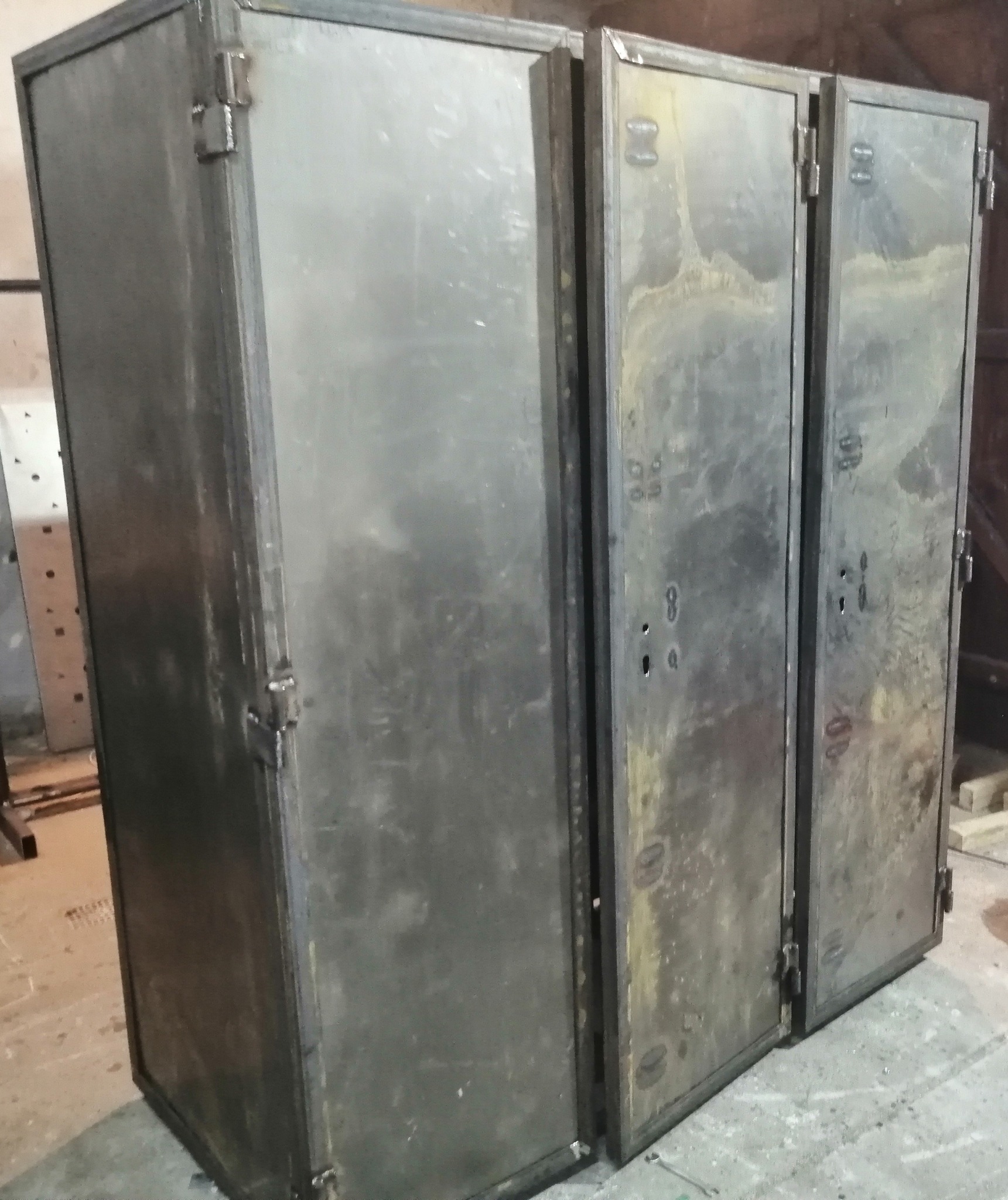 Metalowa szafa z trzema parami drzwi, wykonana ze spawanych profili, widoczne ślady obróbki i mocowania zawiasów.