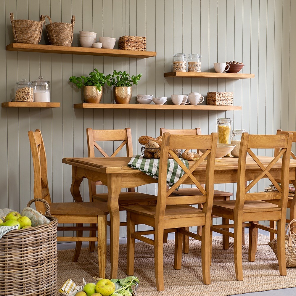 Rustykalny stół i krzesła z litego drewna w jadalni. Na ścianie półki z dekoracjami. W koszu jabłka. Całość w ciepłej tonacji, naturalne materiały.