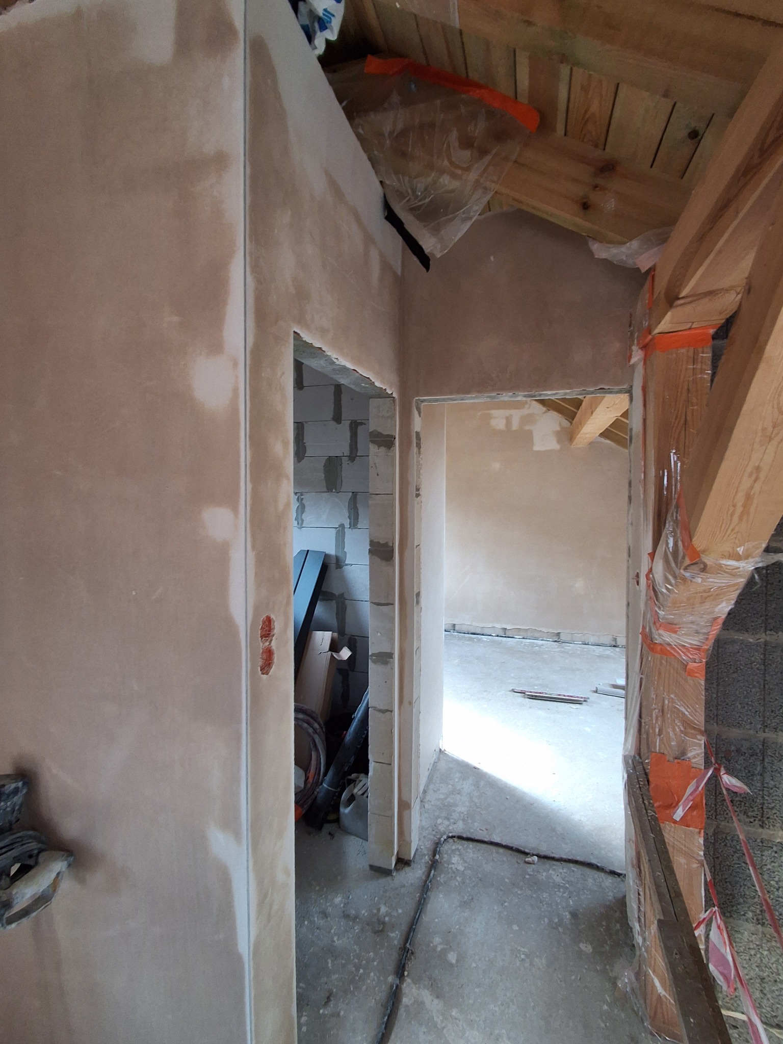 Wnętrze w trakcie prac wykończeniowych w Tucholi: ściany po gładzi, widoczne bloczki betonowe i elementy drewniane konstrukcji dachu, przygotowane do dalszych prac.