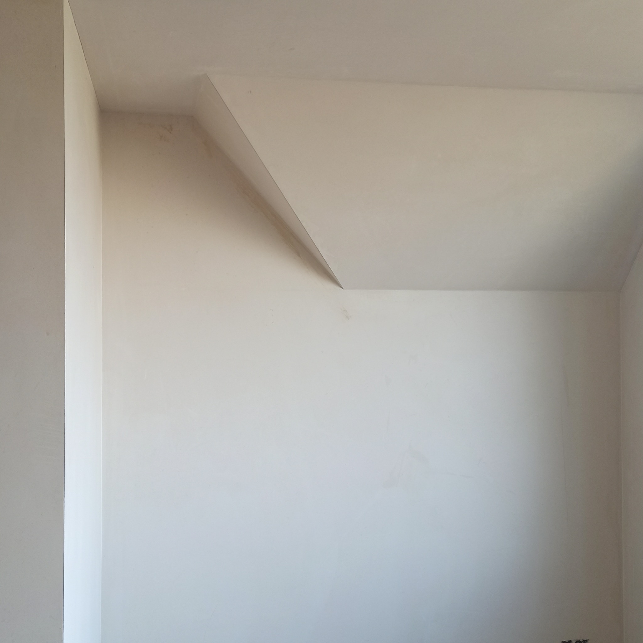 Wnętrze po gładziowaniu: gładkie, jasne ściany i sufit w narożniku pokoju, gotowe do malowania. Widoczne delikatne załamania światła podkreślają równość powierzchni.