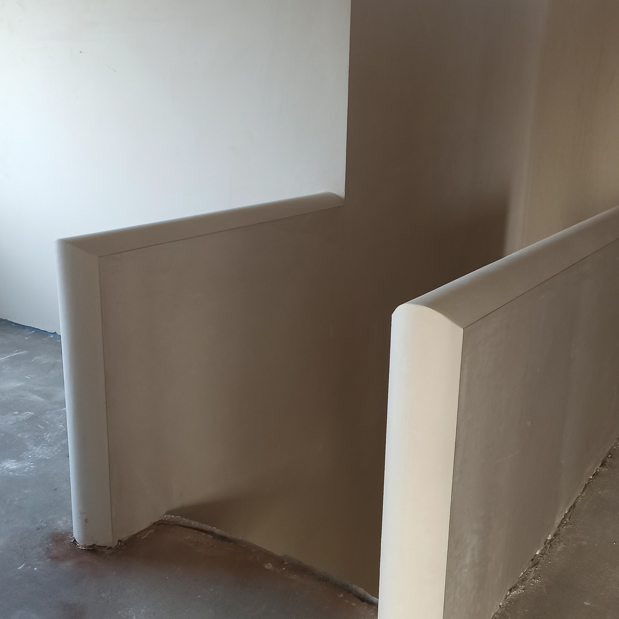 Gładkie, jasne ściany po tynkowaniu maszynowym, z zaokrąglonymi narożnikami schodów. Widoczny surowy beton na podłodze.