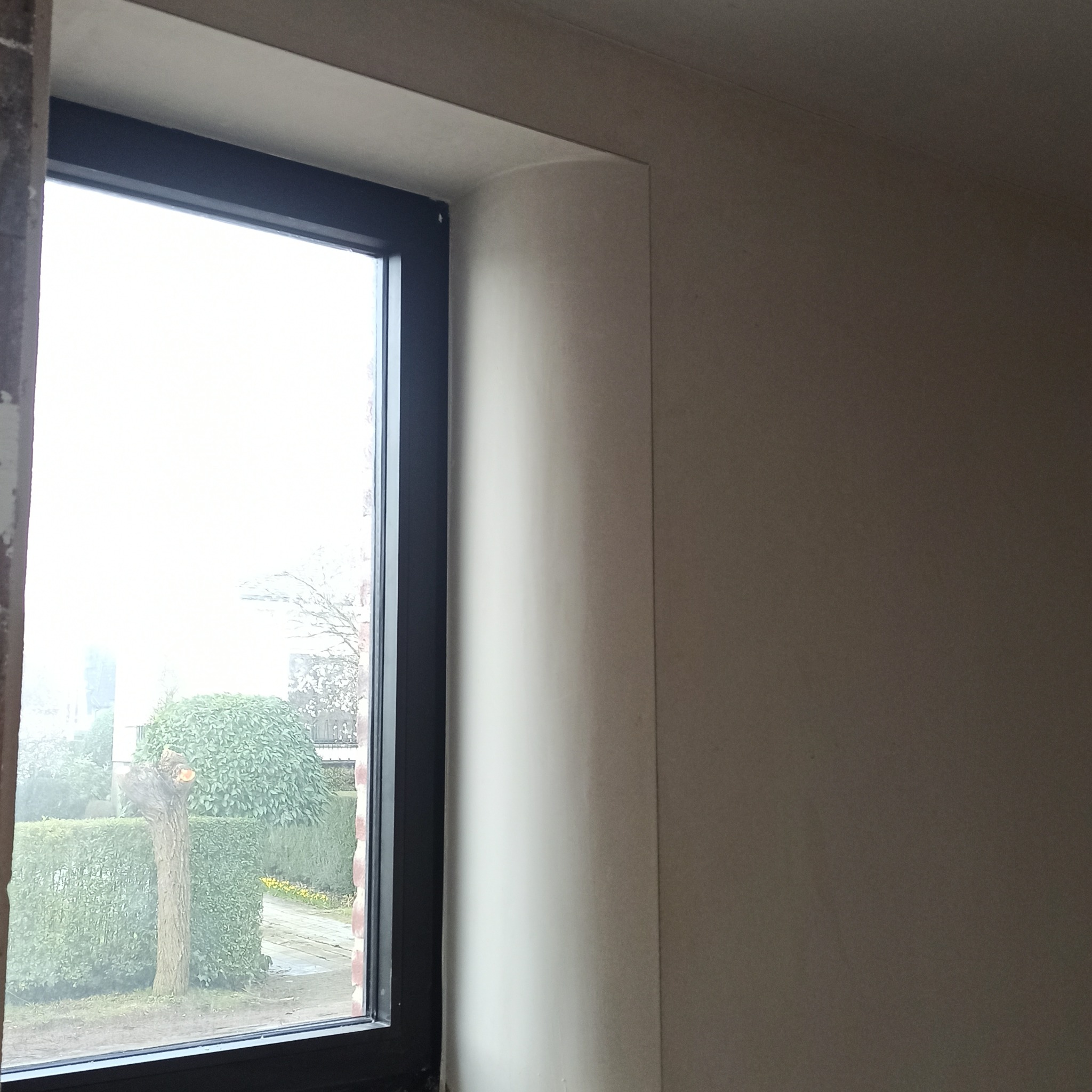 Gładka ściana po tynkowaniu przy oknie w Tucholi. Widoczne zaokrąglone wykończenie narożnika okiennego. Świeżo położony tynk w jasnym odcieniu.